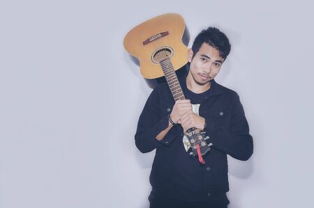 Handsome young man sitting and plays on the acoustic guitar - isolated on white background.の写真素材