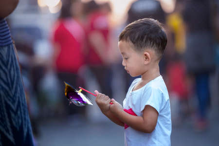 Boy wandering on a walking street in a city holds a toy with a multicolored windmill and stares with interest. Happy moments together.の写真素材