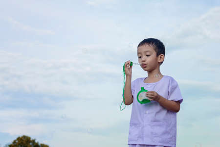 A little Asian boy blowing bubbles, playing with joy and happiness in the beautiful and green nature.の写真素材