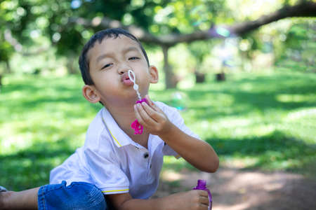 A little Asian boy blowing bubbles, playing with joy and happiness in the beautiful and green nature.の写真素材
