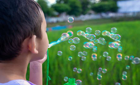 A little Asian boy blowing bubbles, playing with joy and happiness in the beautiful and green nature.の写真素材