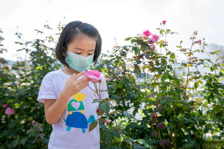 Little girl wore a face mask with the idea of a trip to a beautiful flower garden during the coronavirus, or the COVID-19 outbreak a new normal concept.の写真素材