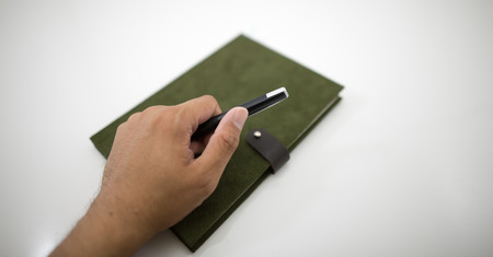 Hand holding a black pen on notebook green velvet.の写真素材