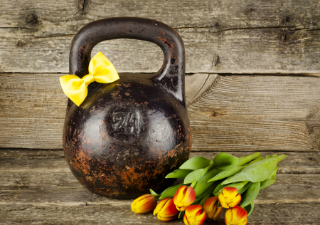 Old kettlebell with a bow on the boards with a bouquet of tulipsの写真素材