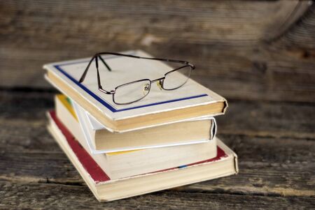 Stack of old books and glasses on a wooden background, shallow dofの写真素材