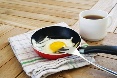 Fried egg in the red small pan and coffee on the wooden tableの写真素材