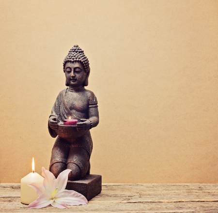 Buddha statue with a candle in hands on a wooden backgroundの写真素材
