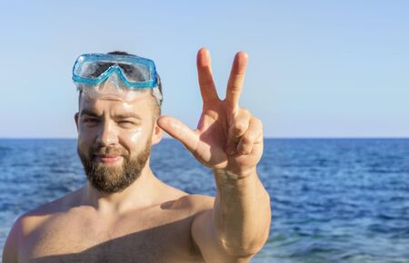 Young adult man with the beard squinting and showing a three-finger salute on the blue sea backgroundの写真素材