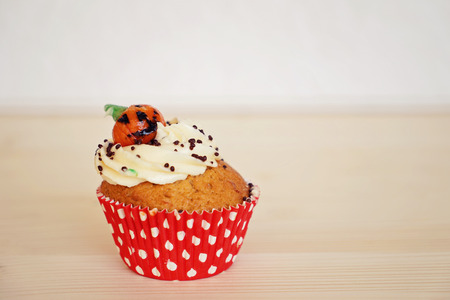 Cupcake decorated with cream and marzipan pumpkin on Halloween on the beige backgroundの写真素材
