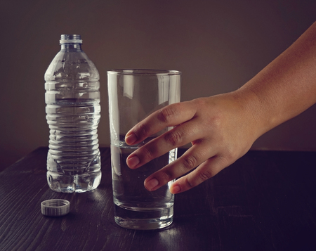 A womans hand takes a glass of water, a glass with clean fresh water and a plastic bottle on the tableの写真素材
