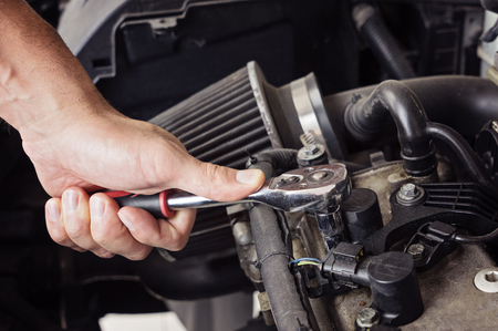A man hand unscrews the spark plugs in the car close up, toned blue