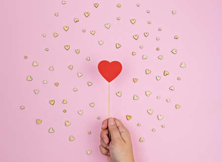 Hand holds large red wooden heart on pink background Valentine's day greeting card conceptの写真素材
