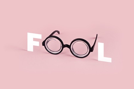 Funny goggles with round glasses on pink background and the word FOOL. April fool's day greeting...
