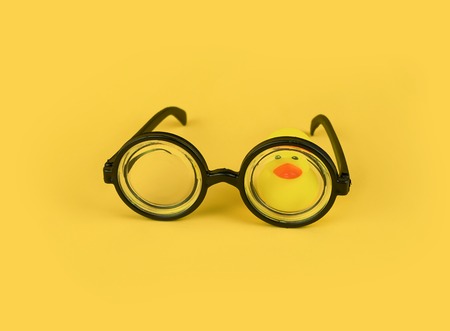Funny goggles with round frame glasses on yellow background and yellow rubber duck. April fools day greeting card concept, education, school time, copy spaceの写真素材
