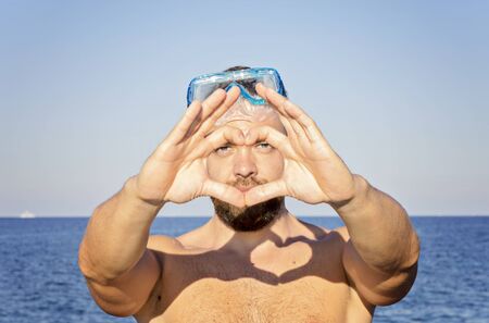 Shape of the heart made by male hands in snorkel mask on blue sea against. Happy vacation concept, selective focusの写真素材