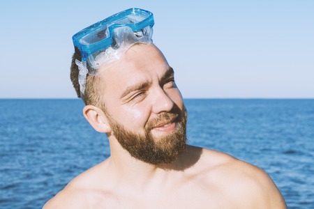 Smiling bearded man suntanning on the beach against blue sea background. Happy vacation concept, selective focusの写真素材