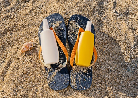 Top view of blue flip flop and two bottle with sun protection spray. Summer skin care concept, flat...