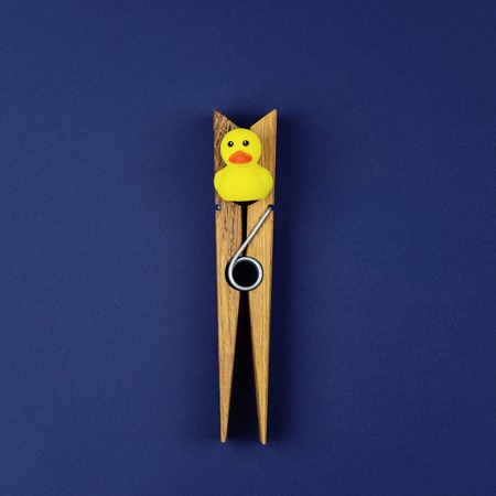 Small yellow rubber duck and large wooden clothespin on blue background. Incarceration and infringement of rights conceptの写真素材