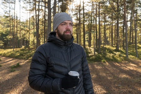 Caucasian bearded man with take away cup of coffee walking in forest and enjoys privacy. Take a...