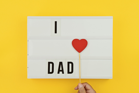 I love Dad text on white lightbox with hand holding wooden heart on yellow background. Greeting card concept to celebrate Fathers dayの写真素材