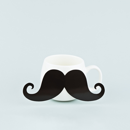 One white coffee mug with large black mustache on blue background, square format, cozy minimalism conceptの写真素材
