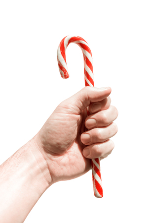 Man's hand holds traditional Christmas striped candy cane isolated on white. Abstract minimal greeting card to celebrate Christmasの写真素材