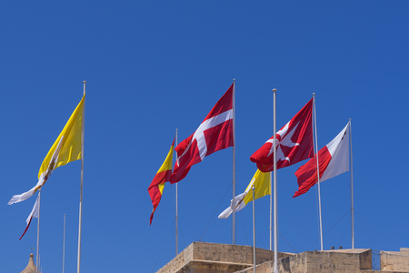 Many different flags over the city of Birgu, Malta against blue clear sky, blowing waving in windの写真素材