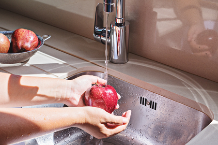 Female hands washing red apple in water stream in kitchen metallic sinkの写真素材