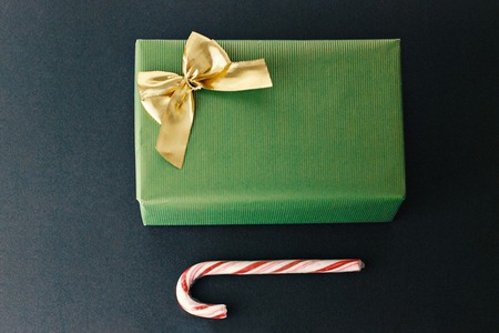 Christmas gift wrapped in green wrapping paper with large golden bow and traditional candy cane on dark backgroundの写真素材