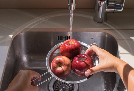 Female hands washing red apple in water stream in strainerの写真素材