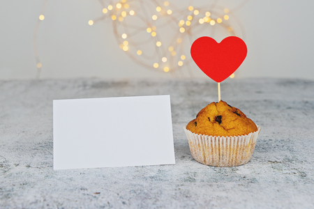 One cupcake with big red hearts and empty Valentine card on light background. Template mockup to celebrate Valentines day, Mothers day and Birthdayの写真素材