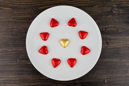 Abstract chocolate candies in hearts shape on white plate on wooden background. Greeting card to celebrate Valentine's dayの写真素材