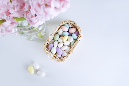 Top view of fresh hyacinth flower in vase with Easter eggs candies in basket on white. Concept for...