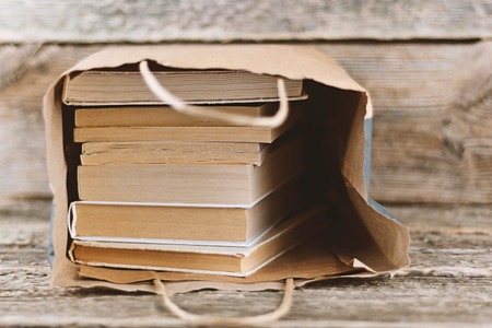 Stack of old books in paper bag on wooden background. Bookstore and Fair Concept sale, World book day, copy spaceの写真素材
