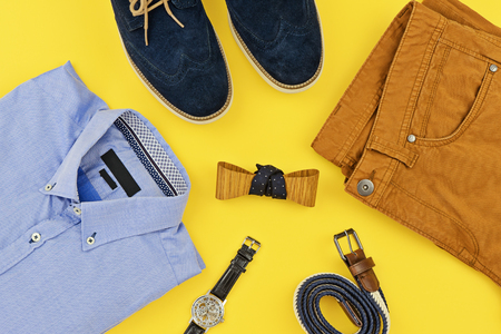 Casual outfits for man clothing with blue shirt, mustard jeans, belt, watch, blue shoes and accessories isolated on yellow background, top view. Trendy fashion male flatlay backgroundの写真素材