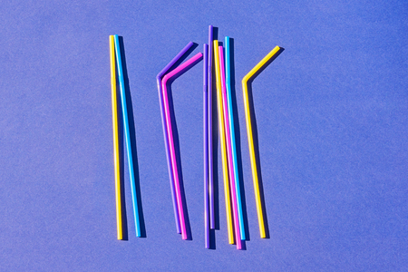 Colored disposable plastic straws on purple background with copy space, top view. Concept of ban on use of plastic tubesの写真素材