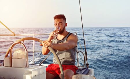 Caucasian white captain man yachting with glass of wine. Summer leisure activity sailing conceptの写真素材