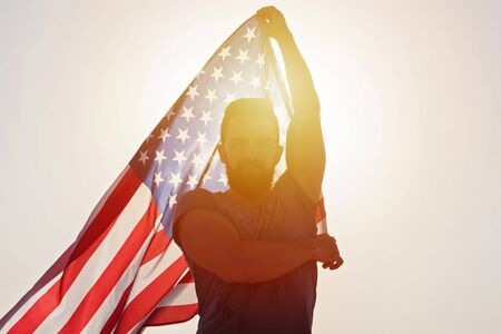 Independence day of United States. Silhouette of adult man with raised hands with American Flag against sunlight. Concept of American people patriotismの写真素材