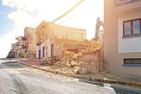 Excavator working at the demolition of an old residential building among other houses. Maltese Excavation and demolition works concept old house with new rulesの写真素材