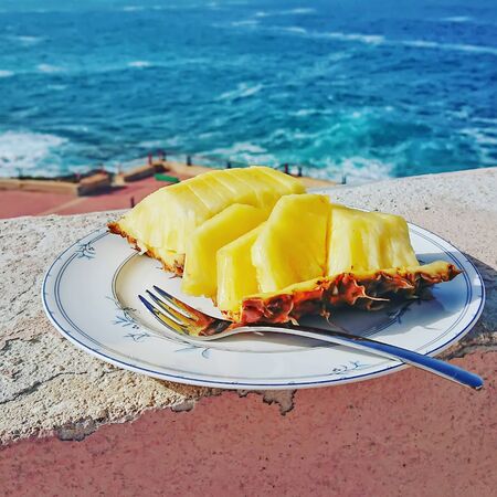 Closeup of ripe and juicy sliced pineapple on plate against blue sea. Summer holiday concept