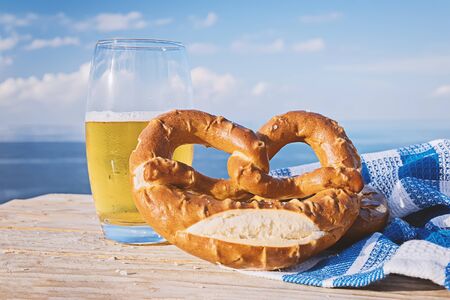 German pretzel and glass of beer in sunlight against blue sky. Salted pretzel is a traditional...