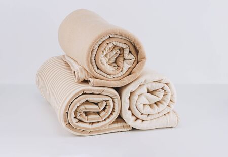 Closeup pile wrapped folded natural beige cotton blanket for kid on white background