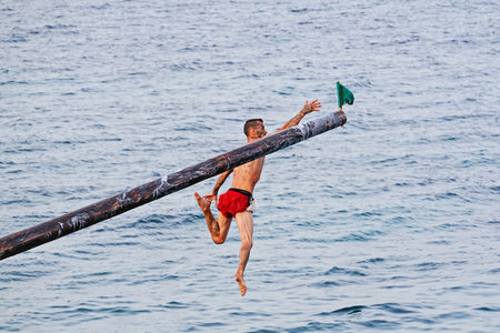 Xghajra, Malta - August 3, 2019: Traditional Maltese game of Gostra, where is Brave local men would try to run up pole and reach one of symbolic flags at top in order to claim prizeのeditorial素材