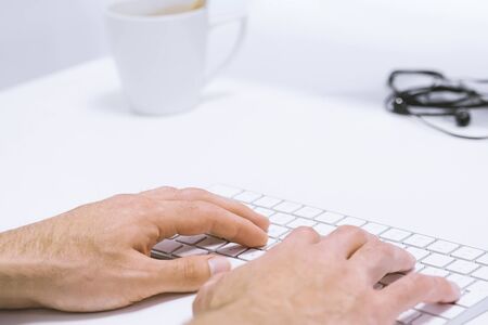 Man's hand typing working on wireless keyboard on white work place, closeup and above view. Light...