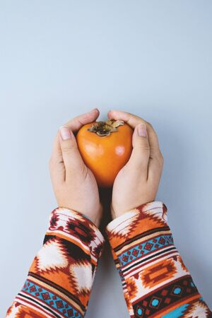 Female Hand sholds ripe persimmon on blue background. Minimal concept for decoration with copy spaceの写真素材
