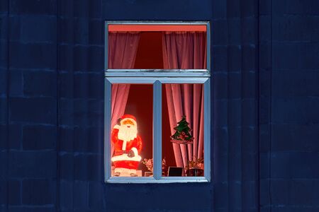 Vintage glowing illuminated Santa Claus in cozy window on Christmas Eve. Classic blue color toned imageの写真素材