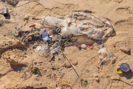 Discarded garbage by wave at beach, cigarette butt, plastic packaging and bottle cork at sandy...