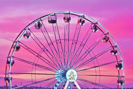Closeup colorful Ferris wheel against sunset pink sky. Abstract cityscape view, motion blur, selective focusの写真素材