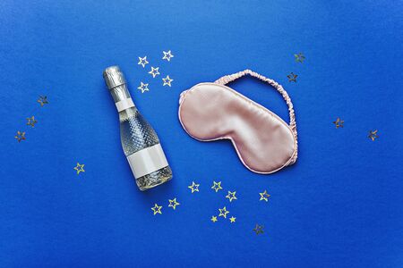 Bottle of champagne and mask for sleeping on blue background, pajama party concept. Valnetine day celebrationの写真素材