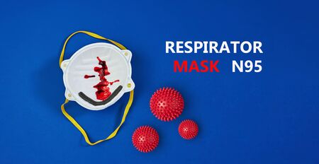 Traces of blood on protective respirator mask N95, blood cough from 2019-nCoV coronavirus on blue background, copy space, illustrative concept, flat layの写真素材